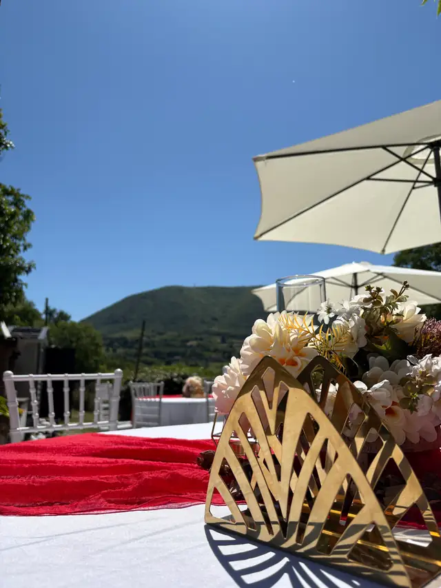 Centrotavola dorato con fiori su un tavolo con drappo rosso, colline sullo sfondo