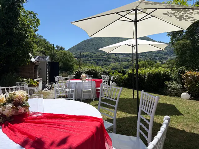 Tavoli allestiti con drappi rossi e fiori, ombrelloni e colline sullo sfondo