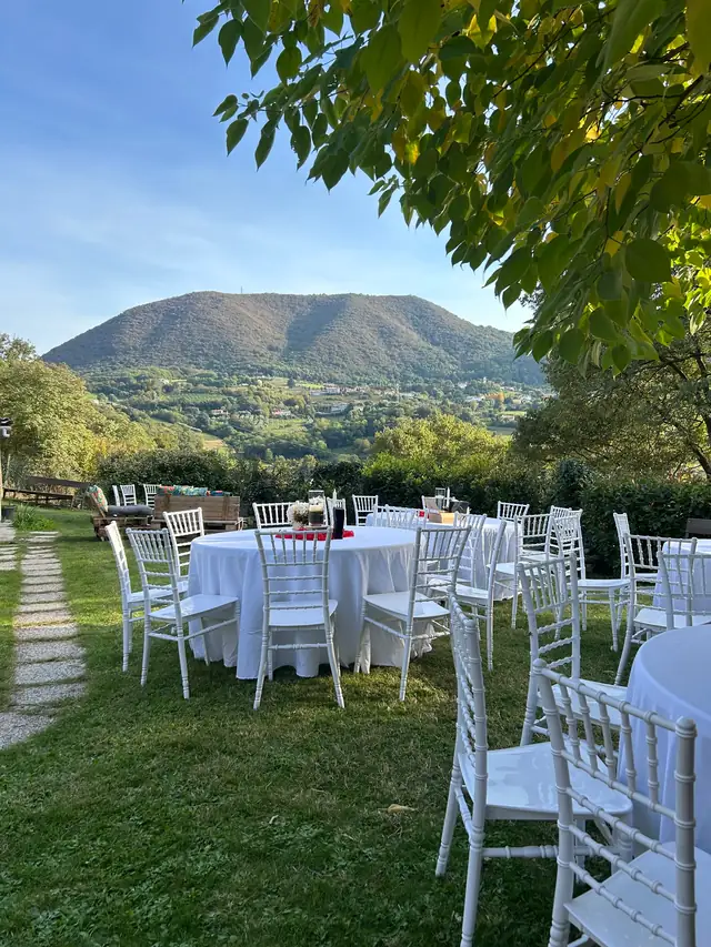 Tavoli rotondi allestiti in giardino con vista sui Colli Euganei