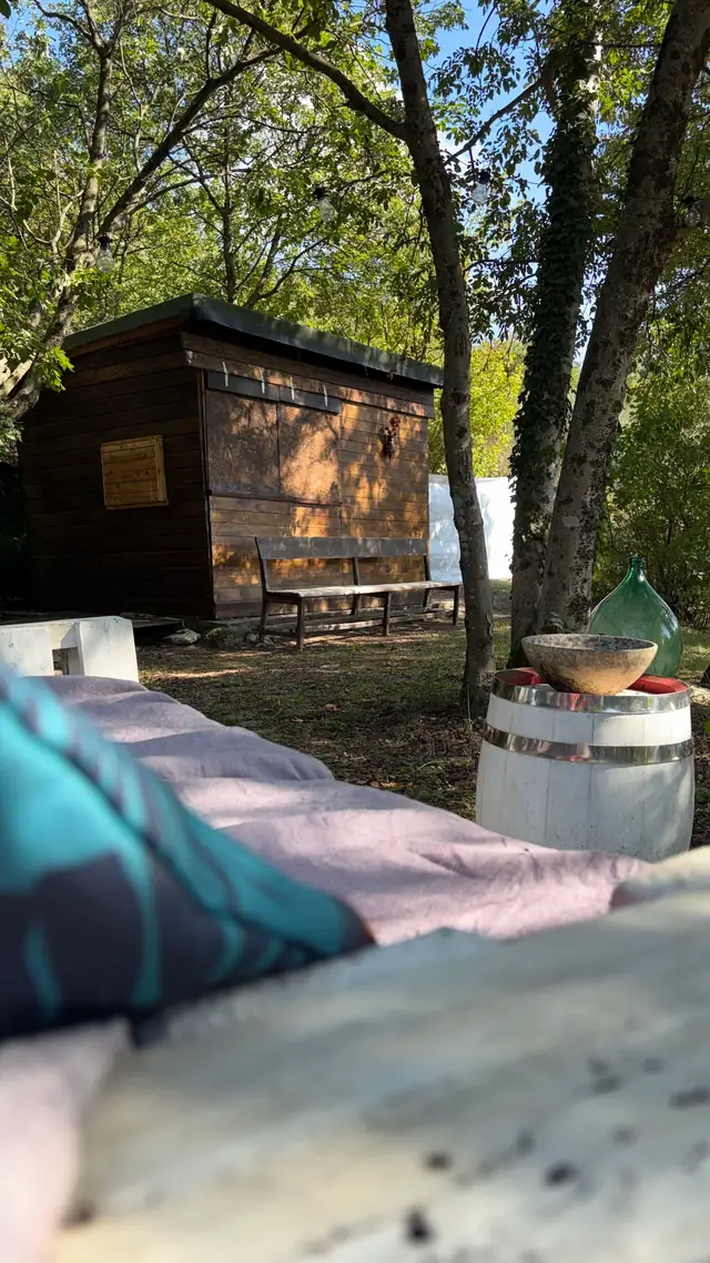 Capanno in legno tra gli alberi del giardino, con cuscini e botte in primo piano