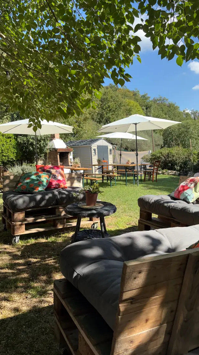Angolo relax con divani di pallet e cuscini, ombrelloni sullo sfondo