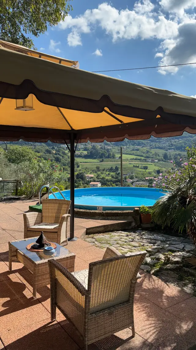 Terrazza con ombrellone e poltrone, piscina e colline sullo sfondo